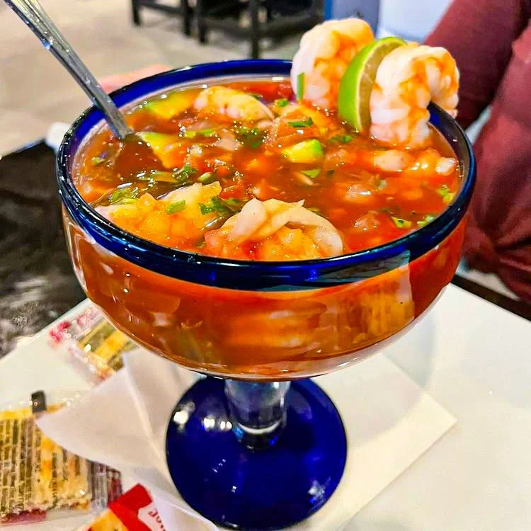 Coctel de camarones - shrimp cocktail in a blue-rimmed margarita glass with lime, avocado and cilantro